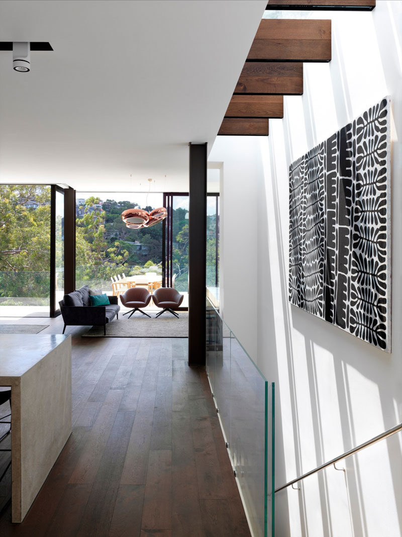 This modern house has stairs with a glass railing, and a skylight filters light down through the staircase.