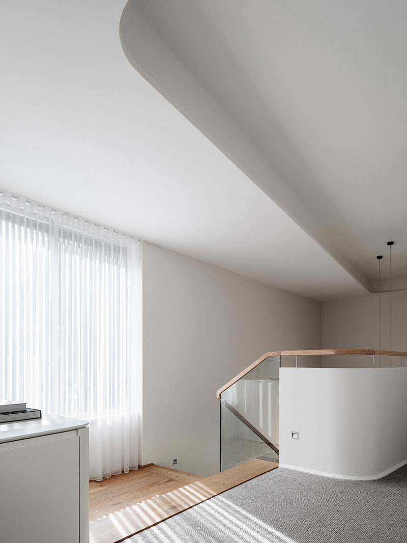 At the top of these modern stairs, there's curved walls and a curved ceiling bulkhead. One the floor the wood from the stairs transitions to a light grey carpet.