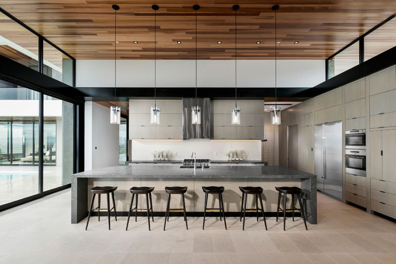 In this modern kitchen, a large island creates plenty of counter space and provides seating for six people. Clerestory windows line each side of the main living room/kitchen and help to make the roof appear to float above the space.