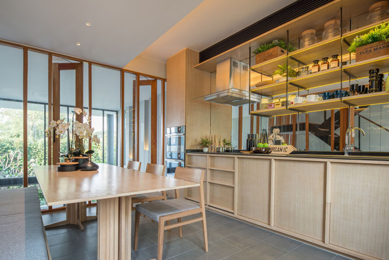 This modern kitchen has light wood cabinets, open shelving and a mirrored backsplash. The kitchen shares the room with the dining table. Floor-to-ceiling windows look over the living room below.