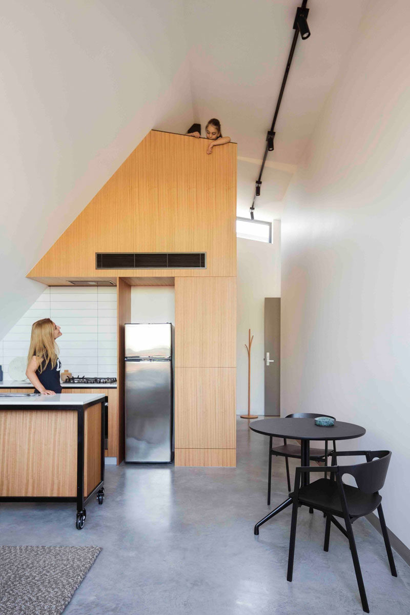 This modern apartment has a light wood and white tile kitchen, with a loft positioned above it.