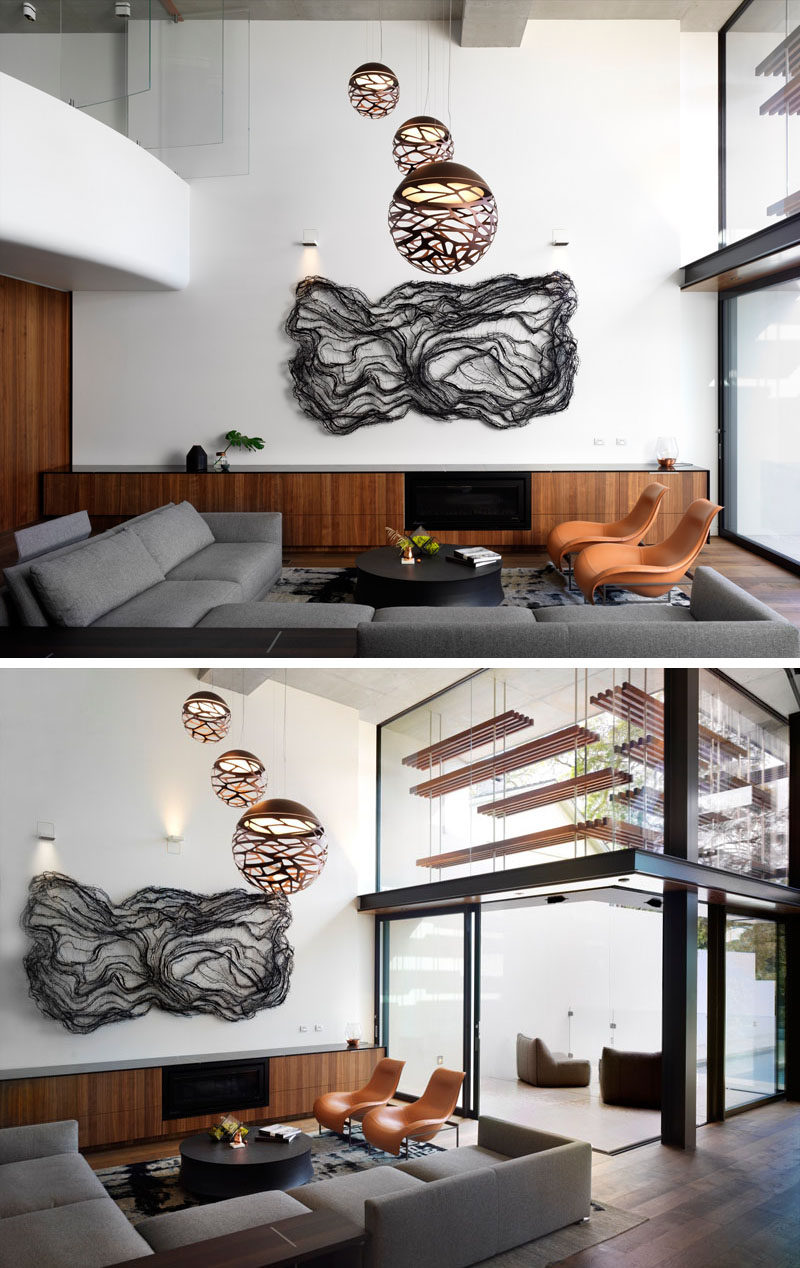 The lowest level of this modern house is home to a large living room that's located in a double height space. A large artwork hangs on the wall and sculptural pendant lights are positioned directly above the couch and arm chairs. Off the living room is an outdoor area.