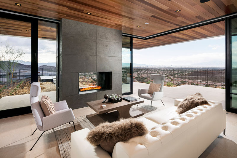 This modern living room with a wood ceiling is focused on the fireplace, and also has access to the outdoor patio area through sliding glass doors.