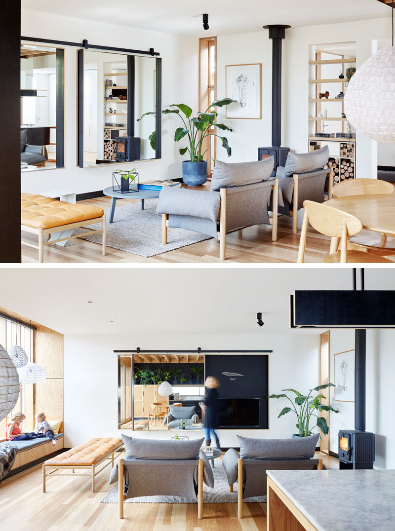 In this modern living room, there's open shelving with firewood storage, and next to the shelf is a wood-burning fireplace. There's also a mirror hanging on the wall, which helps to make the interior seem larger, but at the same time, also hides the television when it isn't being used.