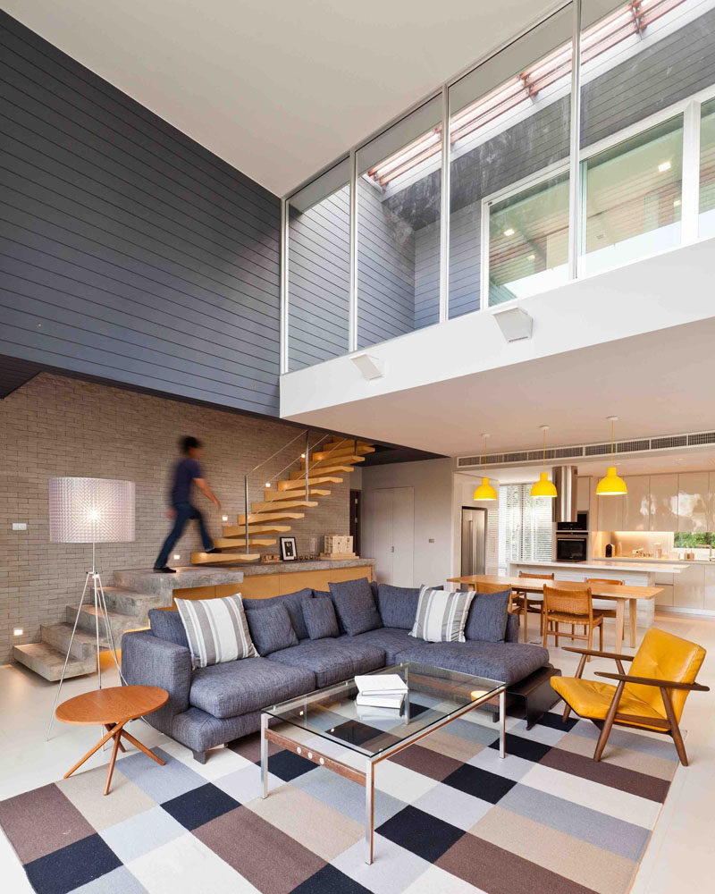 This modern house has a double-height ceiling in the living room, with the living room being anchored in the space by a large checkered rug.