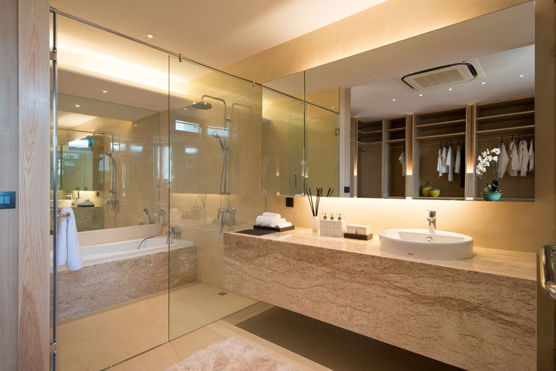 In this master bathroom, a large bath/shower room is enclosed behind a glass wall, and a large back lit mirror makes the bathroom feel even larger. 