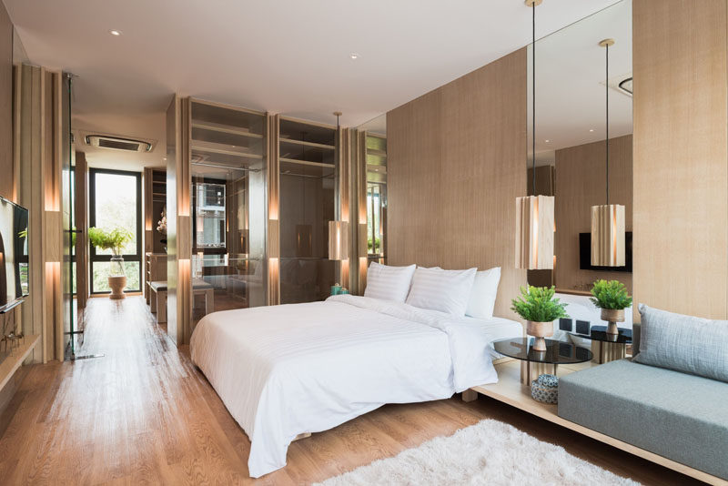 This modern master bedroom is full of light wood and mirrors. Small plants add a touch of nature to the room, and a built-in couch creates a place to relax and read a book.