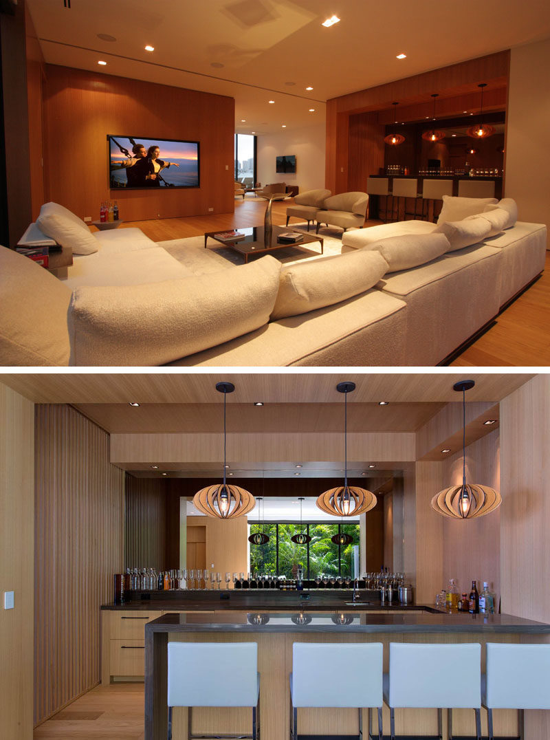 This modern house has a casual living room with a large comfortable couch. Beside the living room is a bar, with a mirrored wall and sculptural wood pendant lights.