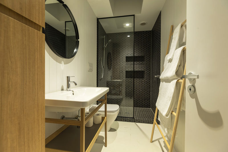 Dark hexagonal tiles fill the shower in this modern bathroom, while a black framed glass shower partition separates the shower from the vanity, that has white tiles and light wood elements.