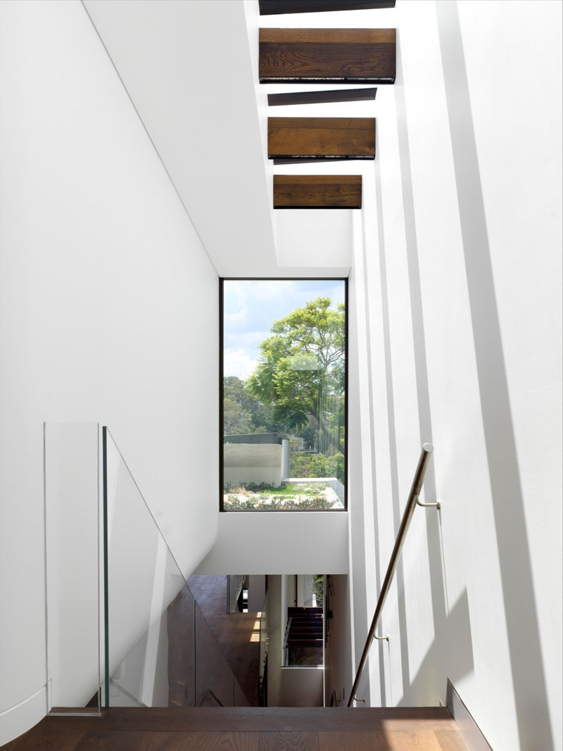 Stairs with a glass handrail and skylight above lead to the next lower level of this house, while a large window provides a glimpse of the green roof outside.