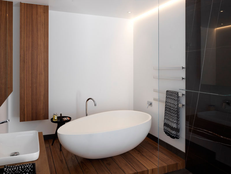 In this modern master bathroom, bright white walls have been combined with wooden elements, while a white standalone bathtub is the focal point.