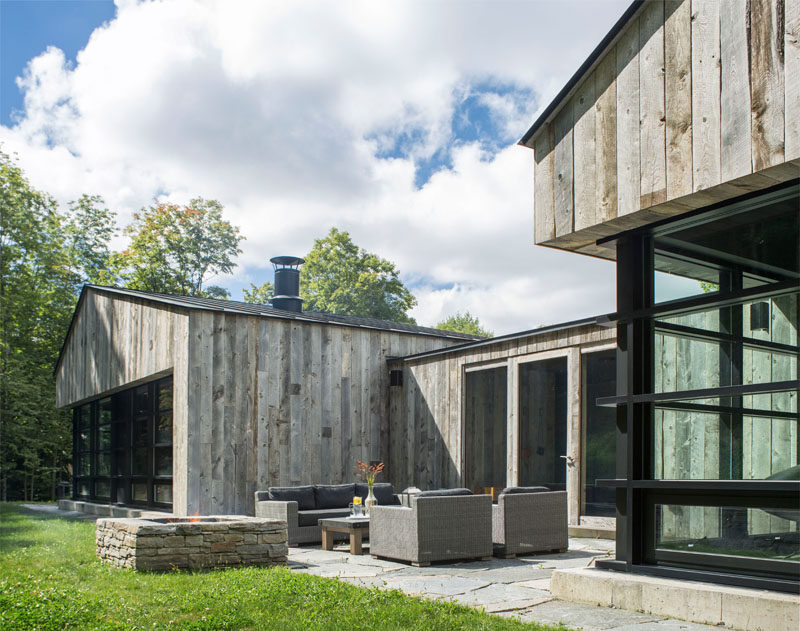 Opposite the entryway in this modern wood house is a door that leads out to an outdoor entertaining space with a couch, a couple of armchairs and an outdoor firepit.