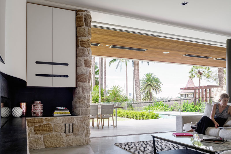 Floor-to-ceiling windows separate the outdoor space from the interiors of this modern house. When opened, the large over-sized windows are concealed within the wall behind the stonework and cabinetry.