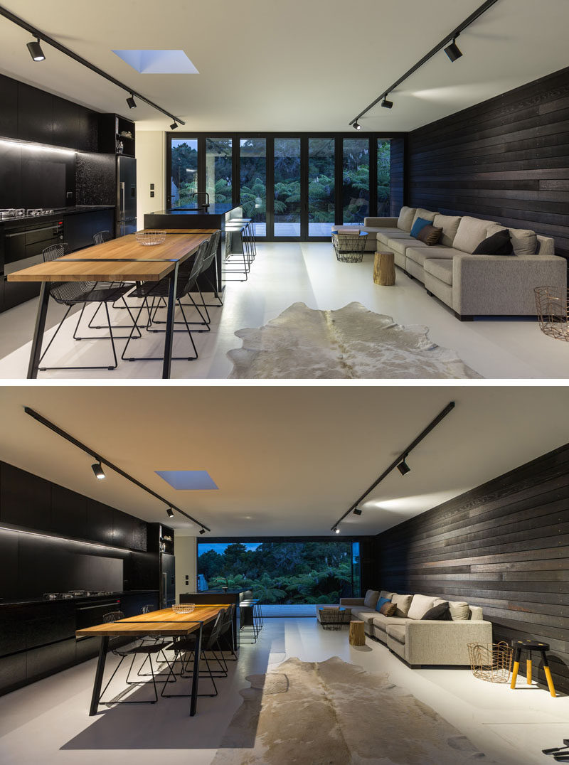 Inside this modern house, the living, dining and kitchen share the same room. The dark wood exterior siding continues through to the interior behind the couch, and compliments the black kitchen on the opposite wall.