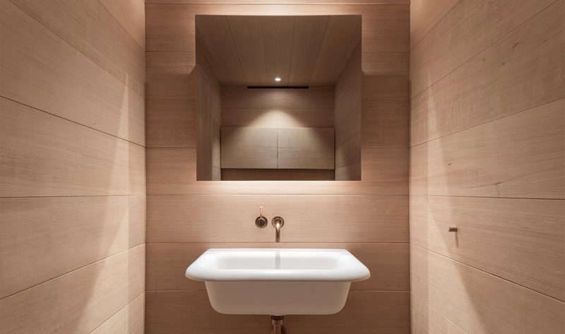 This small bathroom has wood covered walls, a backlit mirror and a simple white sink.