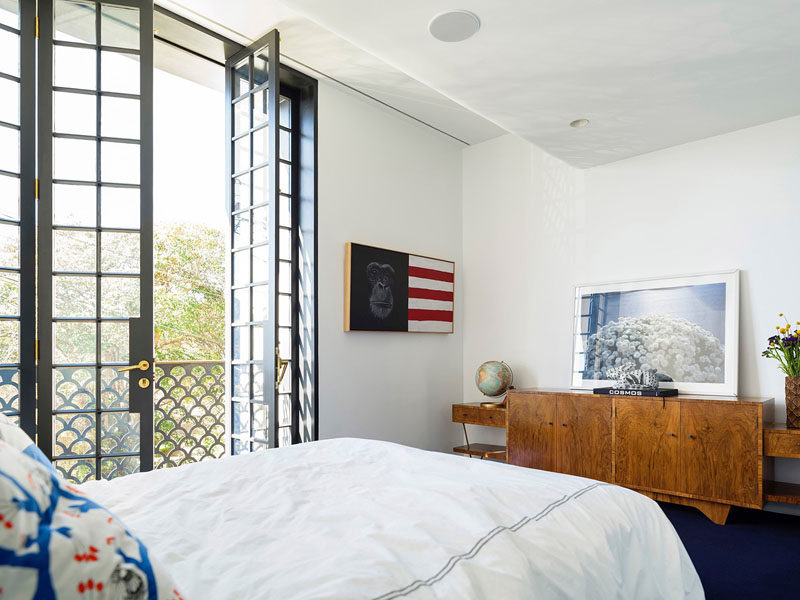 On the second floor of this modern house is a bedroom with tall French doors that open inwards, allowing for fresh air and plenty of light to fill the room.