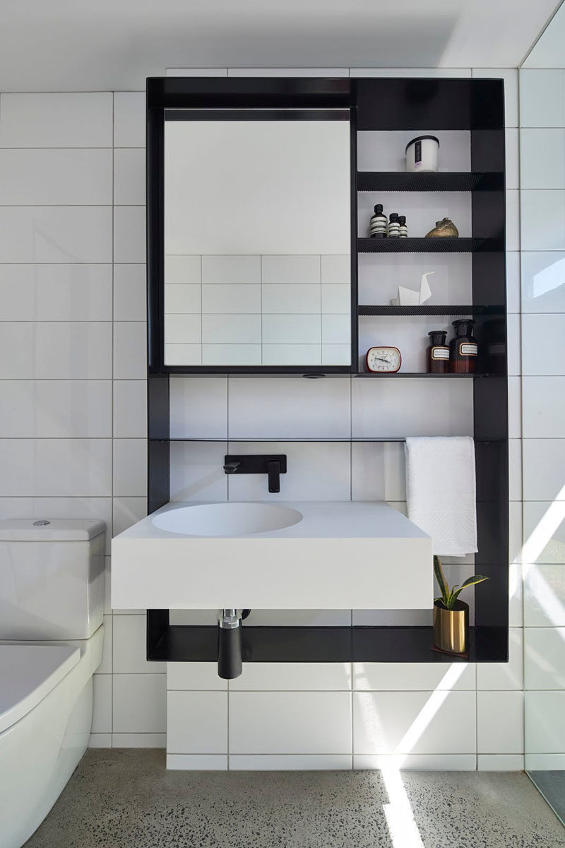 This modern bathroom has white tiles that have been paired with a black wall cabinet for a bold and contrasting look.