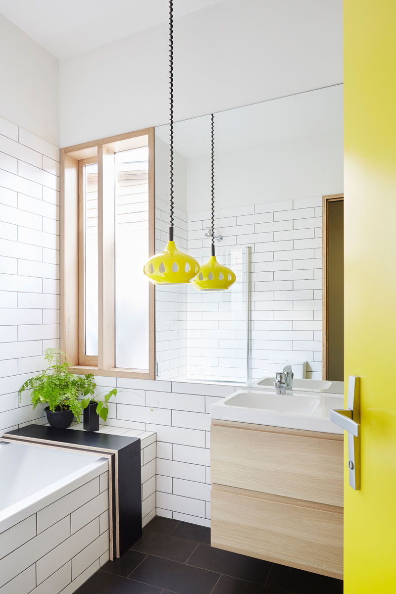 This modern bathroom has a bright yellow door that matches a fun pendant light of the same color, while the remainder of the bathroom is black and white.