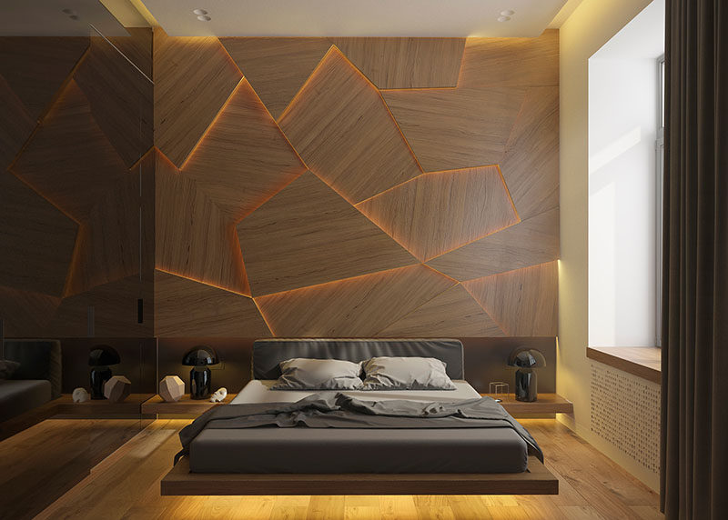 A modern bedroom with a geometric wood panel accent wall and hidden LED lighting.