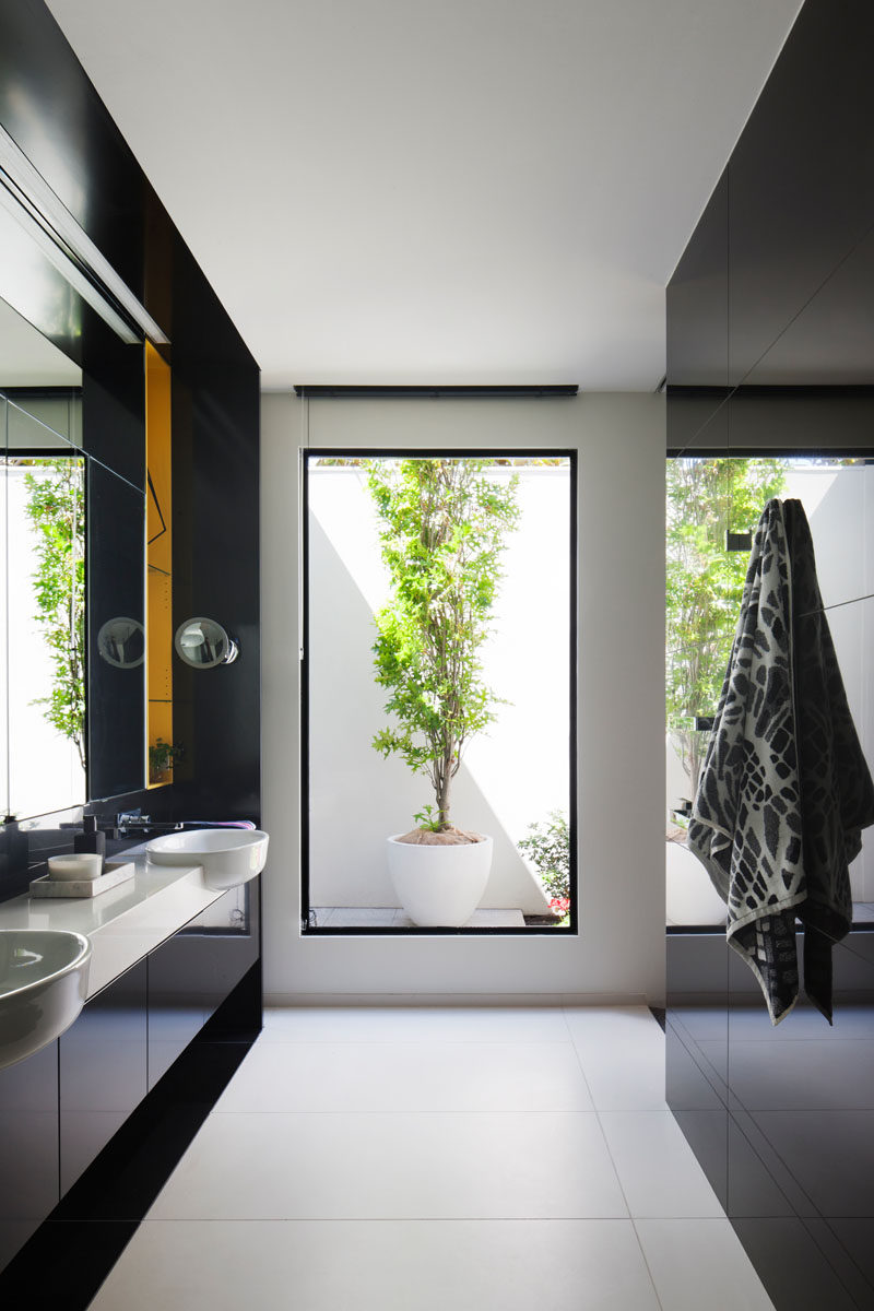 In this modern master bathroom, a tall window perfectly frames a potted plant outside, while a dual sink vanity with black cabinetry and a white counter makes sure there's plenty of room for personal items. There's also a toilet and a walk-in shower.