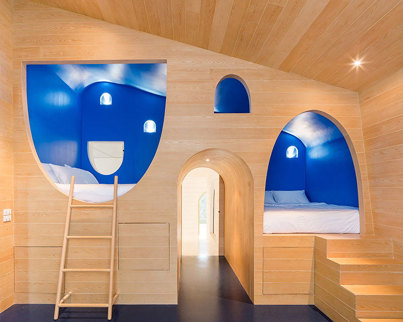 This whimsical yet modern boys bedroom features two built-in beds surrounded by royal blue walls that are built into the light wood wall.
