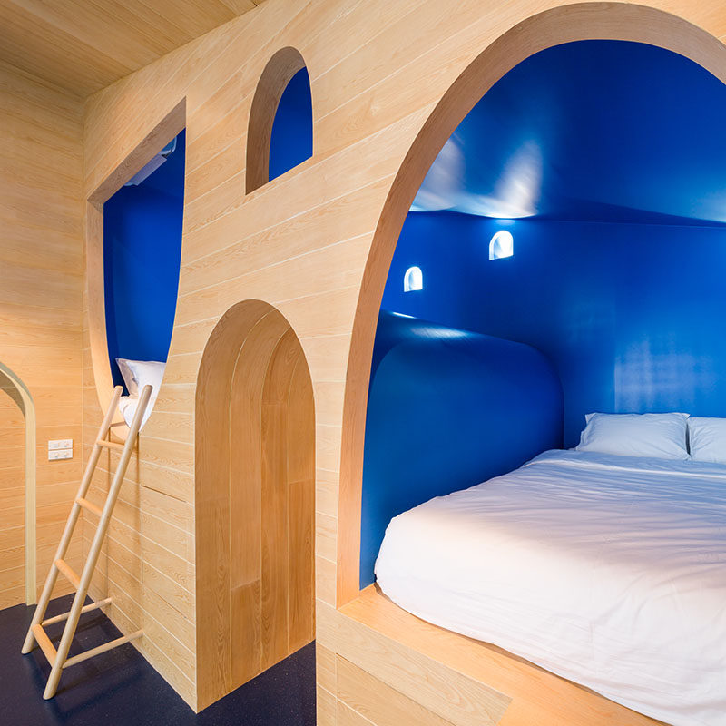 This whimsical yet modern boys bedroom features two built-in beds surrounded by royal blue walls that are built into the light wood wall.