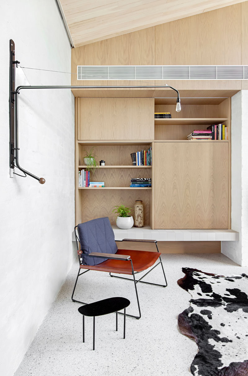 This modern living room has a built-in wood bookshelf with open shelving. A movable metal wall light adds an industrial touch to the room.