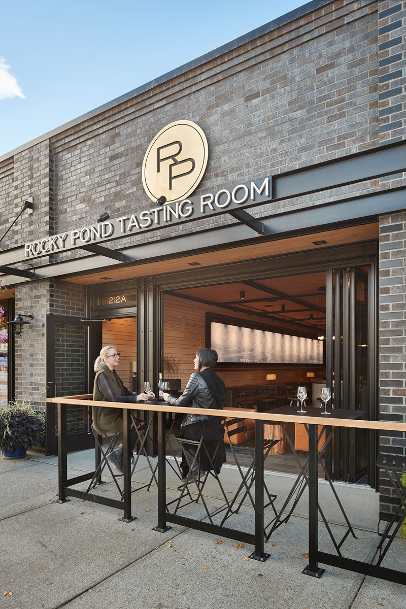 This contemporary wine tasting room has been transformed to an open storefront and a semi-enclosed patio that leads to the interior of the tasting room. The use of casual seating arrangements alongside natural materials and hues, creates a space well suited to experience the taste of their bold wines.