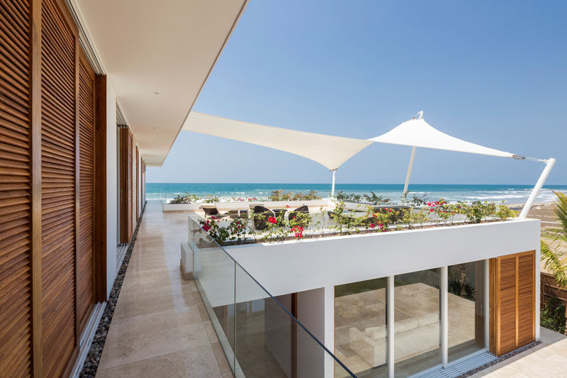On the upper floor of this modern beach house, there's a covered patio area that's protected from the sun by a shade sail. Simply decorated, plants surround the common area creating the effect of a railing-less deck. 