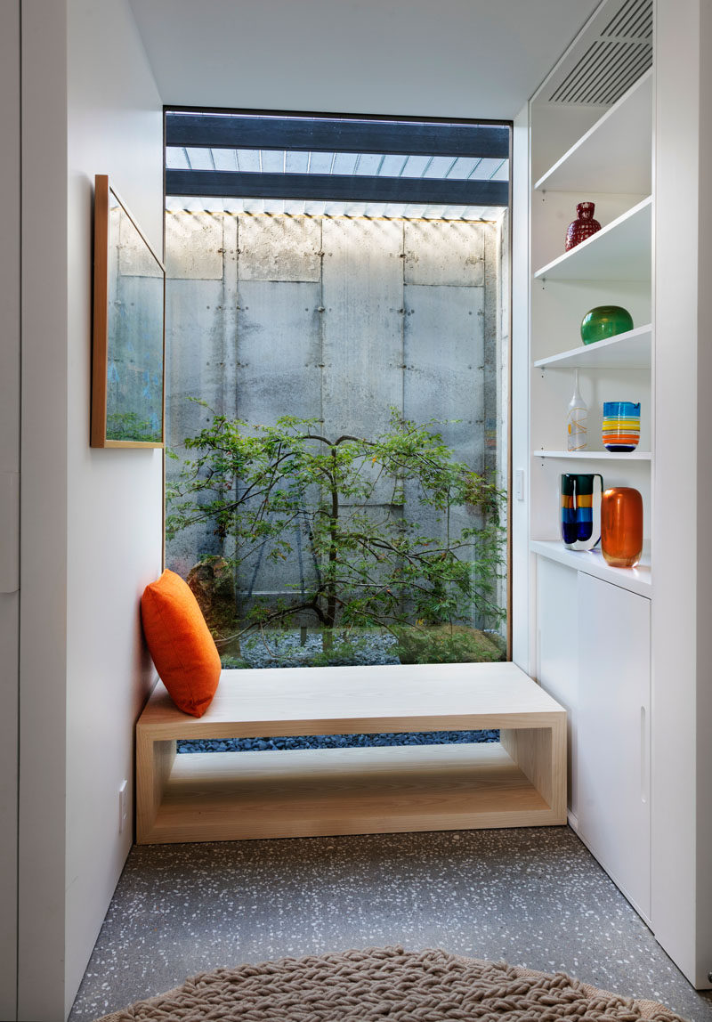 This modern house has a small nook with wood bench seating, a large window and built-in white shelving and storage.