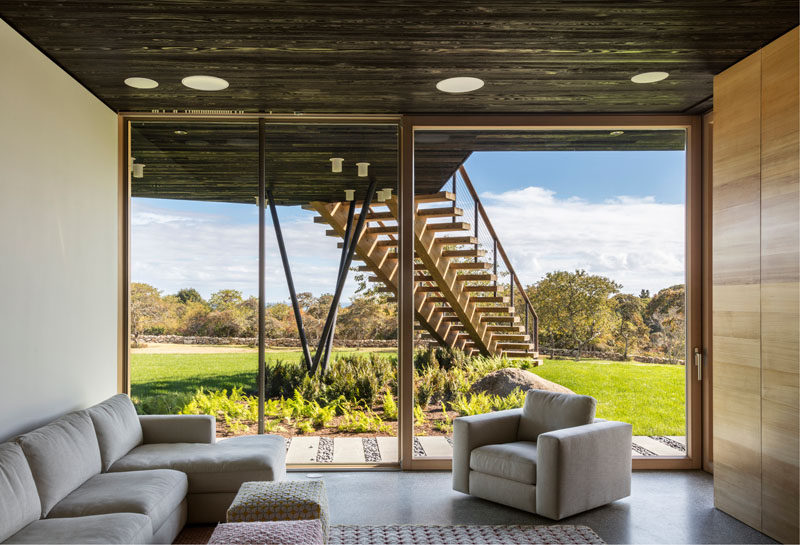 This modern living room has picturesque views through the floor-to-ceiling sliding glass door that also opens up directly to the lawn.