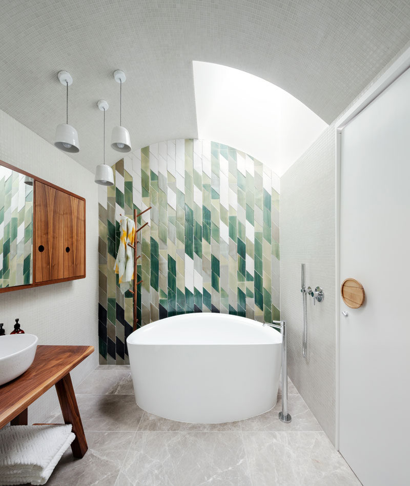 Patterned tiles in shades of green, creates an accent wall behind the bath in this modern bathroom, while a wood wall cabinet and vanity tie in with the oversized circular wood door handle.