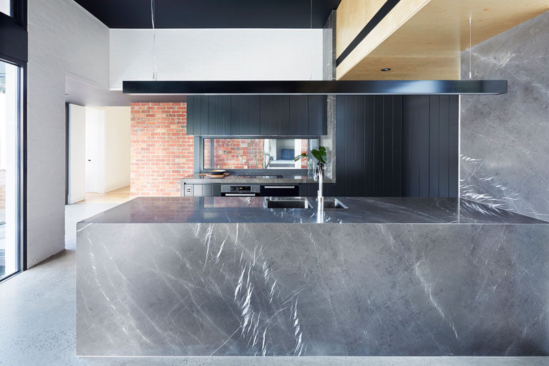 This modern kitchen has a color palette of grey and black, with a long horizontal lamp hanging above one side of the kitchen. 