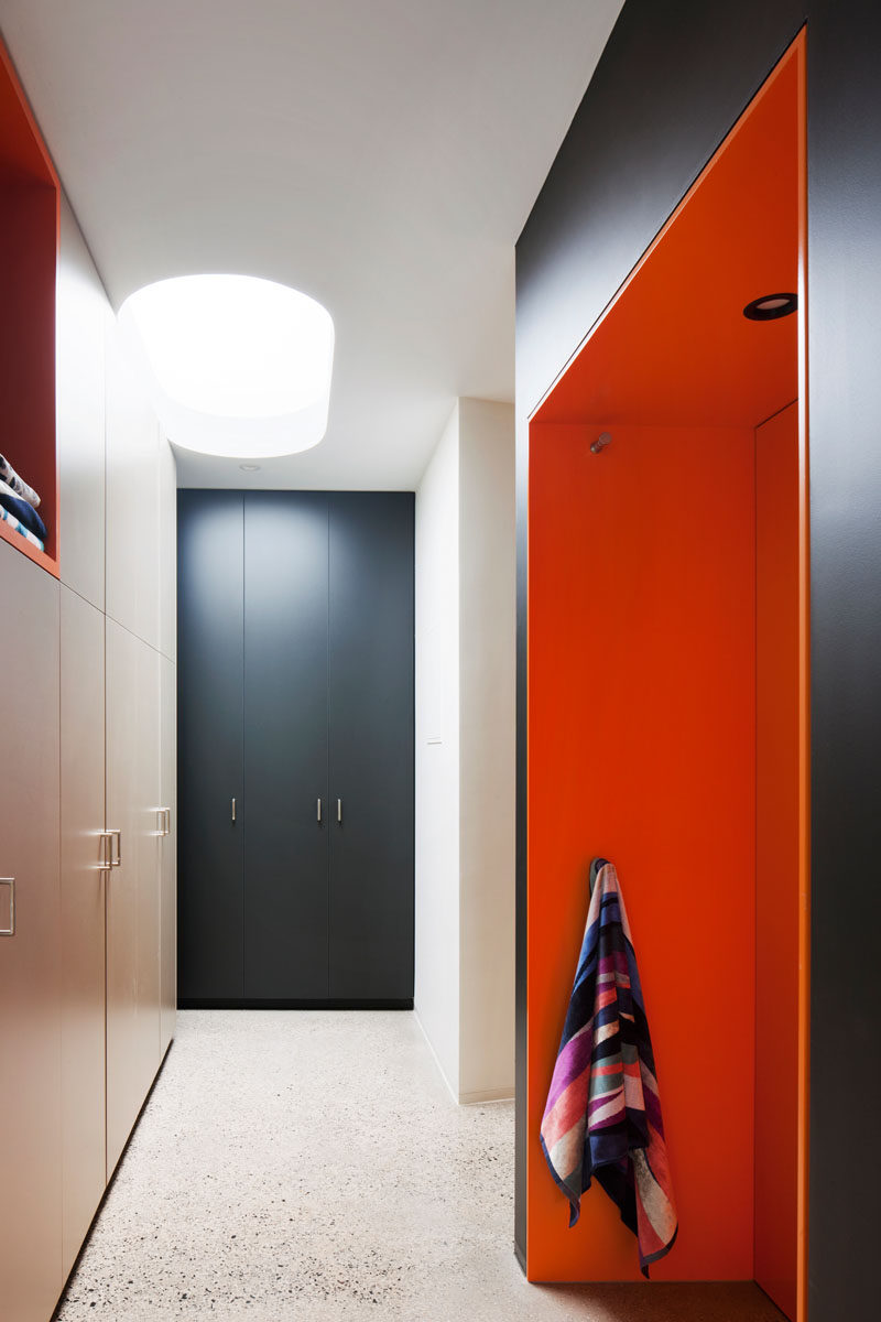 This modern laundry room has floor to ceiling cabinets, and brightly colored orange pockets of open storage areas.
