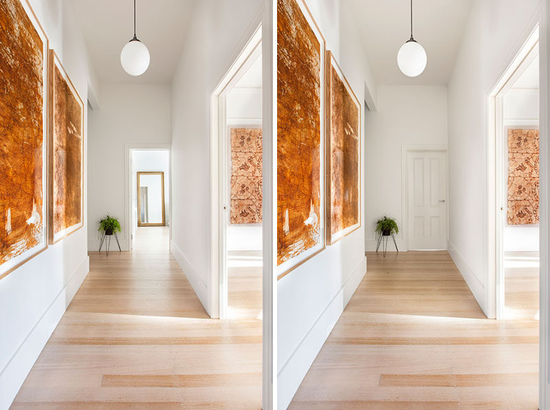 In this contemporary hallway leading to the bedrooms, light wood floors have been paired with white walls, while art and a single plant add touch of color.