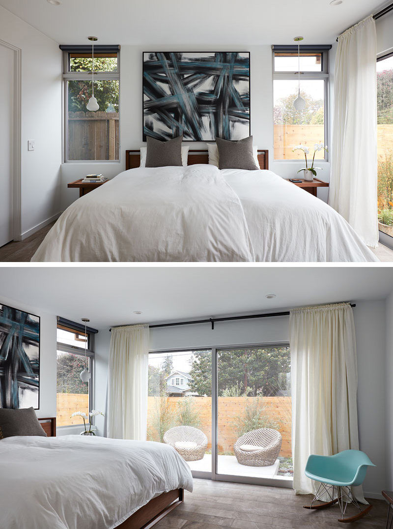 This master bedroom has a pop of color with a bold art piece that matches a blue Eames rocking chair in the corner of the room. The bed faces a large sliding glass door that looks out to a private patio.