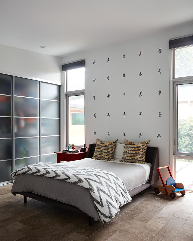 This modern bedroom is designed so that the bed sits between two windows and against a wall with decorative motifs. The closet is accessed by a set of sliding doors.