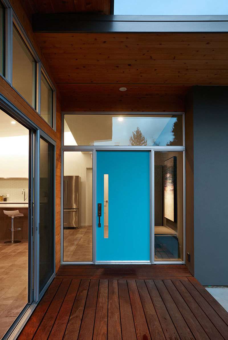 The electric blue door of this house is framed by glass windows, making the entrance of this modern home look larger