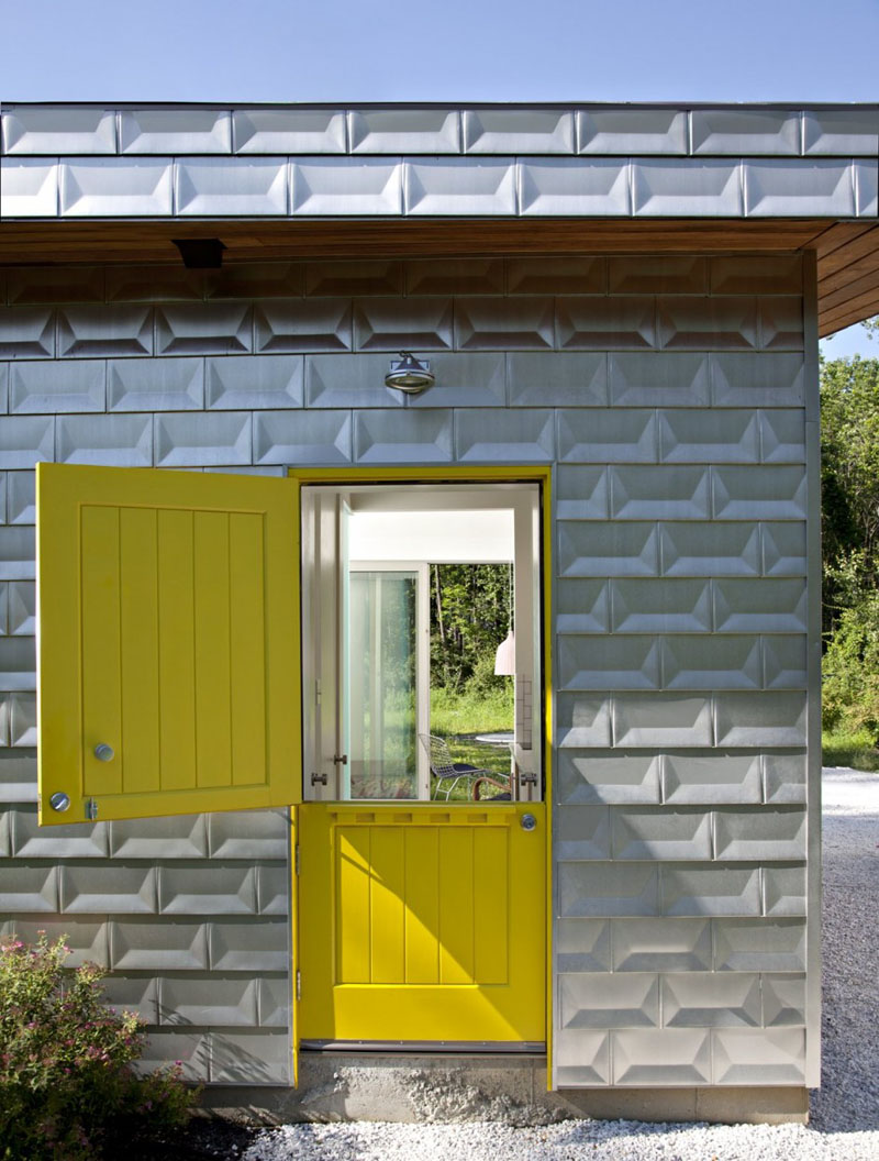 The cottage-style yellow front door that can be opened two ways, bounces color off the brick-like, matte aluminium exterior of this modern house. 