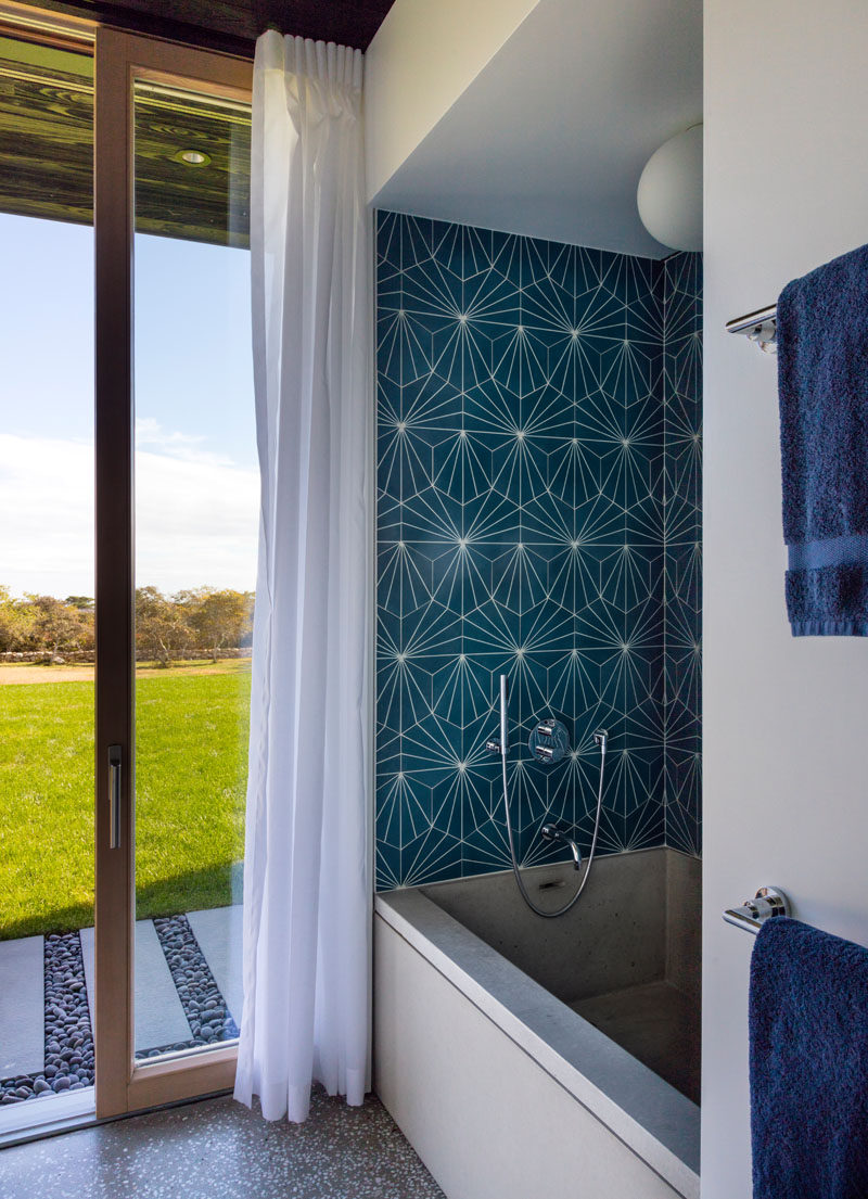 In this modern bathroom, colorful blue patterned tiles have been used to highlight the bath and add some color to the room, while a sliding glass door provides direct access to the backyard.