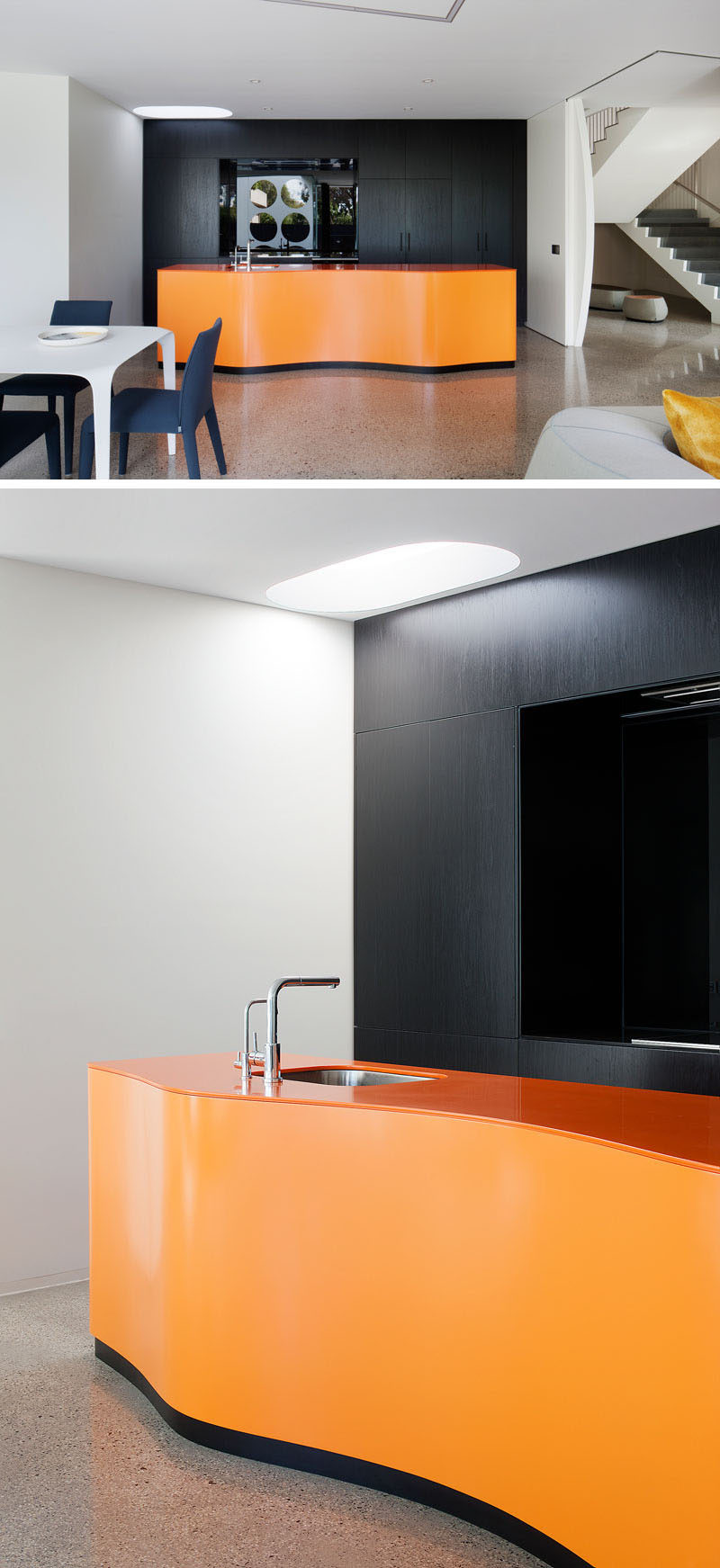 This boldly colored modern kitchen has a curved orange island, while the black cabinets, with an integrated fridge, provide a strong contrast and help to make the color of the island 'pop'. The flooring throughout the house is a hand-crafted polished concrete floor.