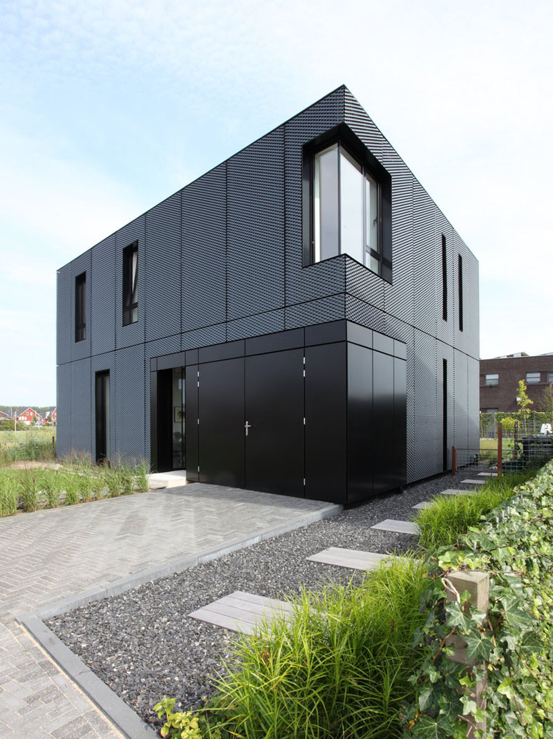 Black metal siding on the exterior of this home gives the cubic house an even more modern appearance and contrasts the greenery surrounding it. #ModernBlackHouse #BlackHouse #BlackExterior #BlackArchitecture