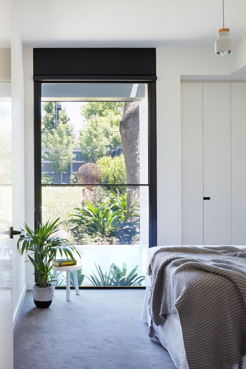 This modern bedroom features a tall black framed window that highlights the sculpture in the garden.