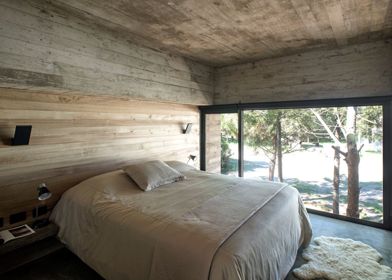 This modern, minimally decorated bedroom with a partial wood accent wall, has an elevated view of outside through the large framed window.