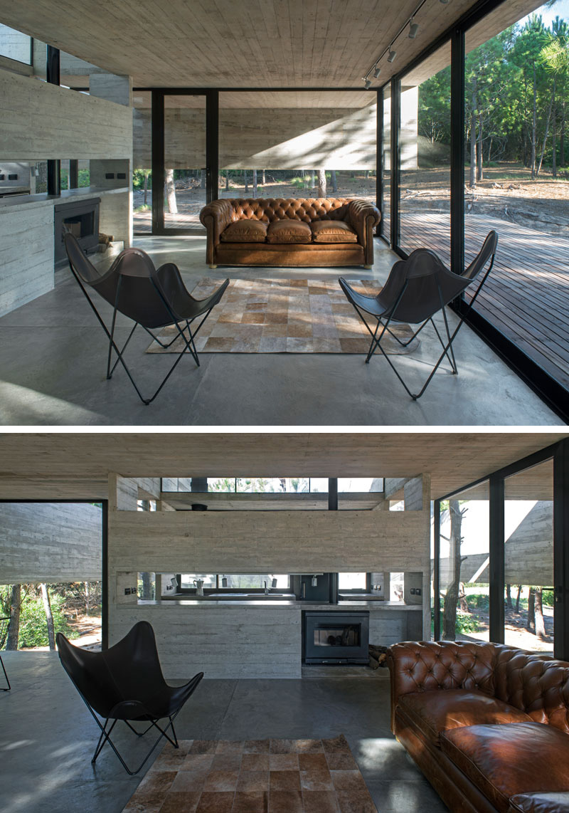 This modern living room is minimally decorated with the floor-to-ceiling windows being the most important aspect in the room. A brown upholstered couch sits beside a black fireplace.