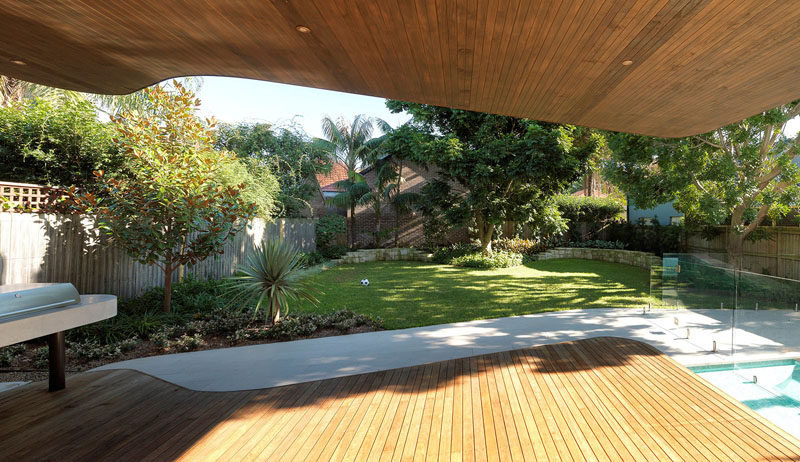 This modern house extension has a cantilever that provides shade to an outdoor space. A Blackbutt wood deck with a ceiling covered in Western Red Cedar has a bbq area off to the side, and a grassy backyard.