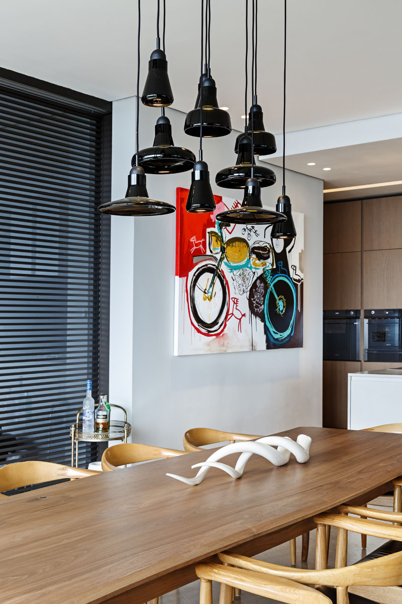 This modern dining area has a large wood dining table with light wood chairs, and glossy black pendant lights