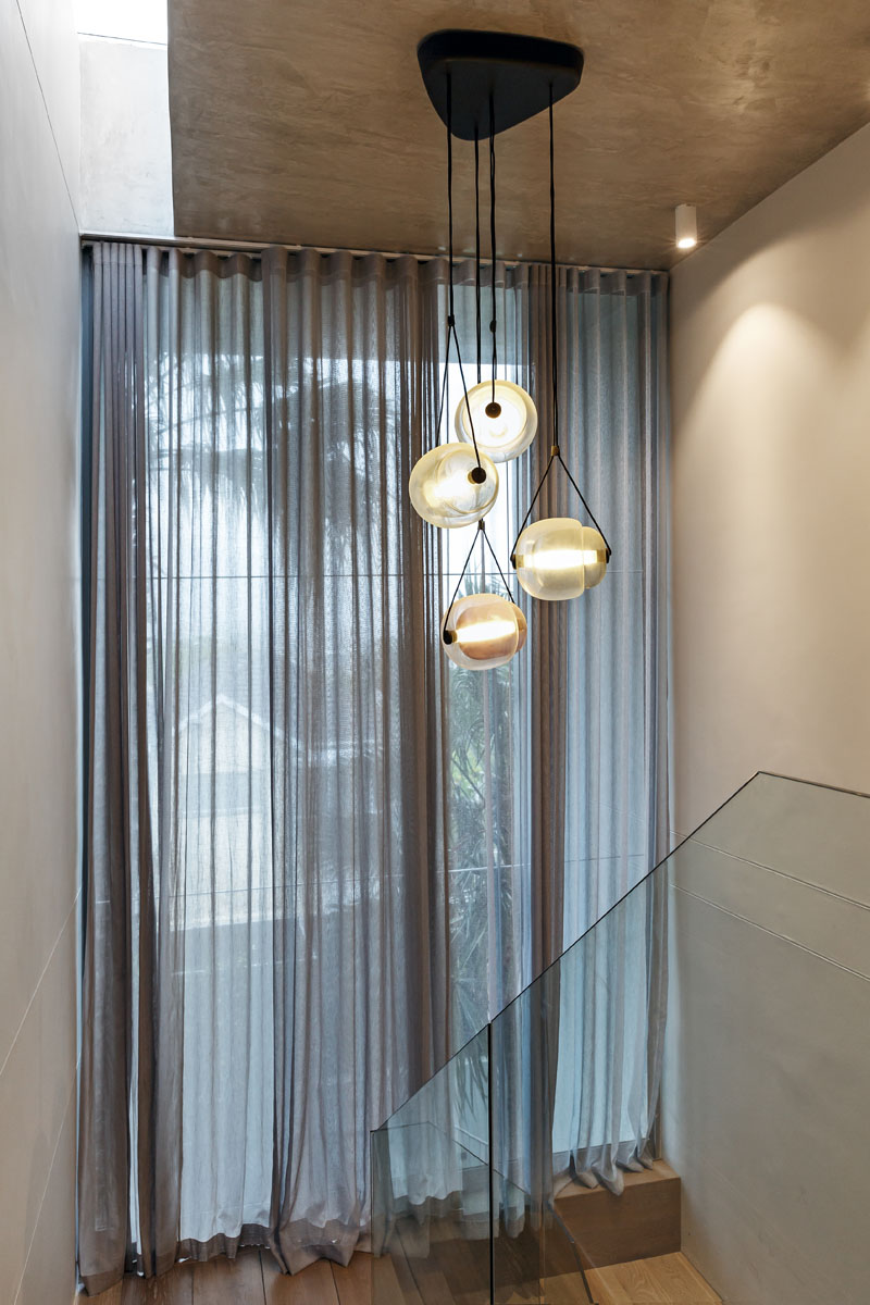 This modern stairwell has a glass hand railing staircase, a floor-to-ceiling window, and a set of large pendant lights.