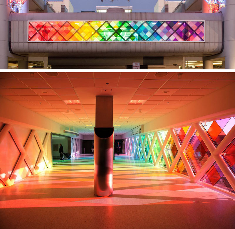 Large panels of colored windows line one side of this airport walkway, making it feel as though a person is walking through a rainbow.