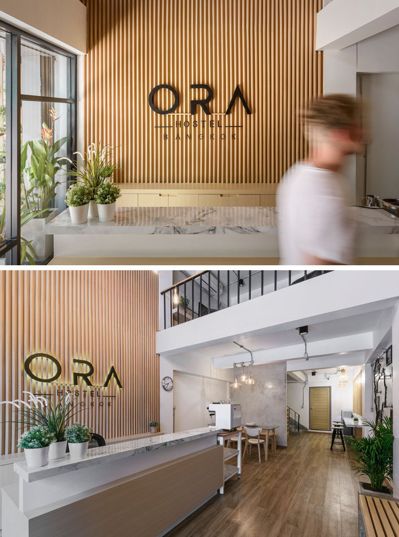 Inside this modern hostel in Bangkok, there's a small reception area with a double-height wood accent wall. Further into the reception area, there's multiple seating options for meeting friends.